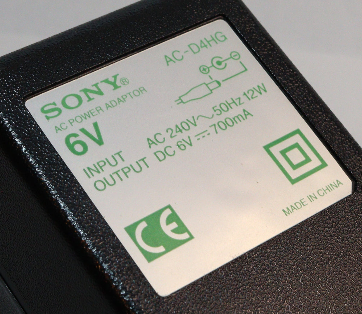 A black Sony 6V power adapter with a white label and attached black power cord, photographed on a light gray surface.