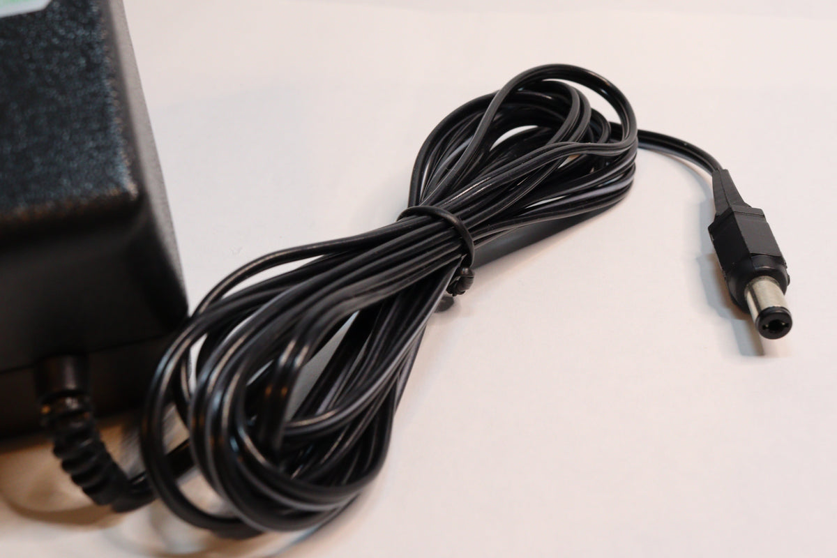 A black power adapter with a coiled black cable and a barrel-style connector, photographed on a plain light background.