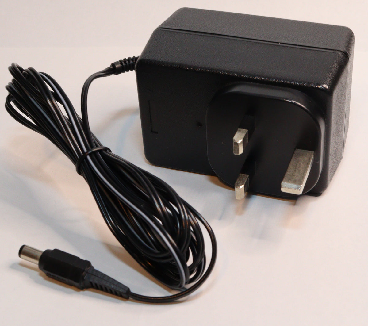 A black rectangular power adapter with a UK three-pin plug and a coiled black power cable, photographed on a plain white background.